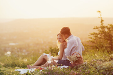 Couple in love on a white plaid take a picnic against the backdrop of a sunset in the mountains. Beautiful couple is enjoying picnic time at sunset. 