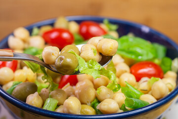 spoon with chickpeas with leaves, olives and tomatoes in a blue bowl