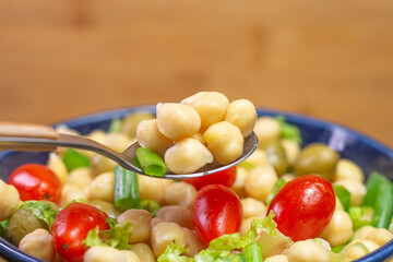 spoon with chickpeas with leaves, olives and tomatoes in a blue bowl