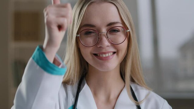 Caucasian smiling happy millennial woman doctor in glasses nurse orthodontist looking at camera dental smile showing thumb up recommends vaccination immunization success glad good sign like gesture