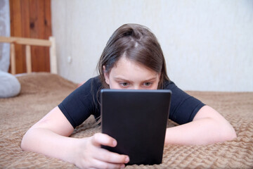 Schoolgirl girl on   bed at home with   tablet.