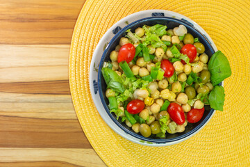 top view of chickpeas with leaves, olives and tomatoes in a blue bowl on the table