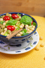 spoon with chickpeas with leaves, olives and tomatoes in a blue bowl on the table