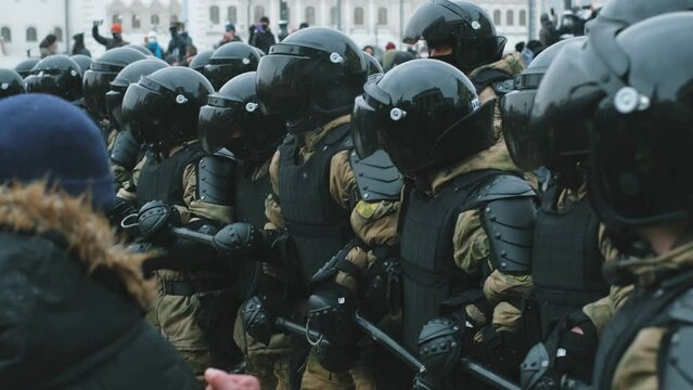 Riot police team with tinted visor on helmets. Policeman officers in rushing attack of protesting crowd on streets. Protesters on demonstration under police units offensive. Pushing enforcers line.