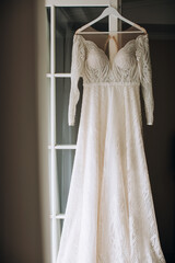 A beautiful white lace dress for the bride hangs on the door of the hotel