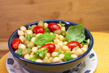spoon with chickpeas with leaves, olives and tomatoes in a blue bowl on the table
