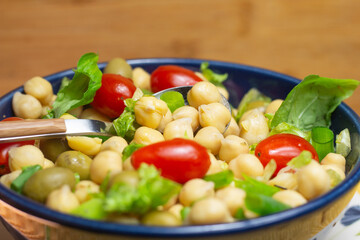 spoon with chickpeas with leaves, olives and tomatoes in a blue bowl
