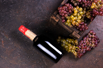 Obraz na płótnie Canvas Ripe sweet grapes in wooden box and wine bottle on dark background. Flat lay, top view image with copy space.