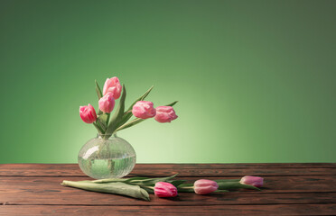 pink tulips in glass vase on green background