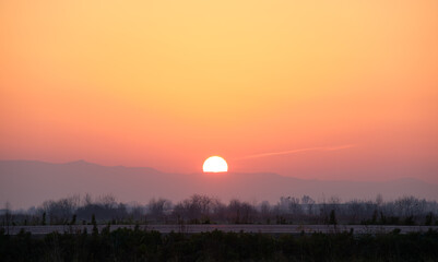 Beautiful evening panoramic landscape with bright setting sun over distant mountain peaks and asphalt road in front at sunset