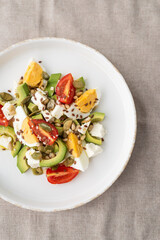 Healthy egg and avocado salad. Salad for breakfast with tomato, avocado, feta, pine nuts, sesame, flax seeds and boiled egg on a concrete background