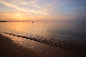 Calm sea shore with crushing waves on sandy beach at sunrise