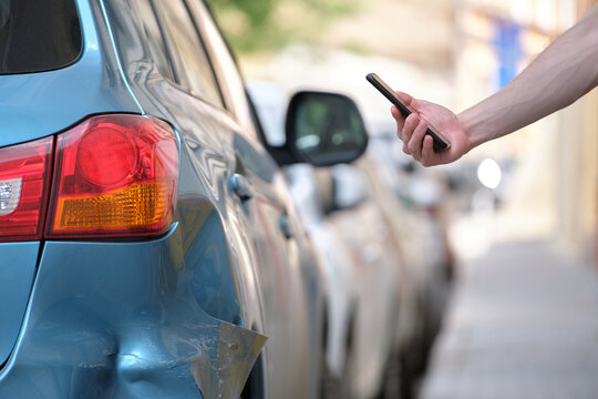 Driver hand photographing on sellphone camera dented vehicle on street side for insurance service after car accident. Road safety concept
