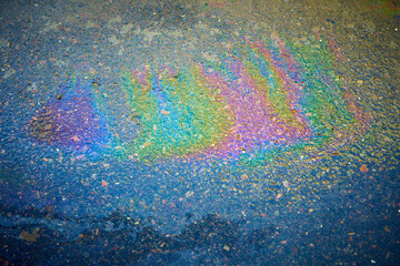 Oil stain on an asphalt road in a puddle in sunlight. Colored spots of gasoline on an asphalt road