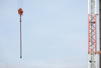 Prace budowlane: podnoszenie siatki stalowej przy pomocy dźwigu budowlanego podczas budowy biurowca na tle błękitnego nieba.