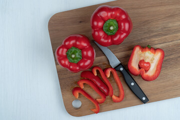 wooden board with sliced red peppers, whole peppers, kitchen knife on a marble table ,top view, copy space