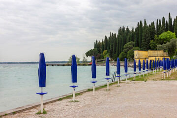 Fototapeta na wymiar Lake Garda beach with cypress trees, Italy, Lombardy