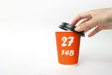 February 27th. Day 27 of month, Calendar date. A woman's hand open black plastic cap of red disposable cardboard coffee paper cup with Calendar Date. Winter month, day of the year concept.