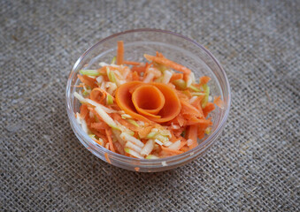 Salad of carrots and apples in a transparent bowl on a canvas tablecloth