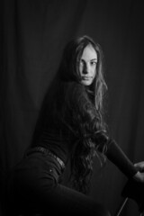 Black and white portrait of a beautiful girl with very long hair kneeling on a stool looking at the...