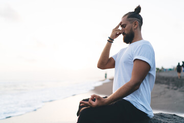 Calm Caucasian man keep praying during daytime for pranayama at seashore enjoying leisure in Indonesia, young male yogi meditate in lotus pose searching soul enlightenment and mindfulness