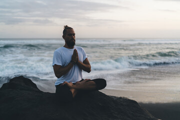 Fototapeta na wymiar Young balanced male breathing in namaste asana during holistic healing and retreat practice for feeling vitality, Caucaisan man enjoying hatha therapy and enlightenment meditation workout near ocean