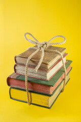 4 stacked books tied with a jute rope levitating on yellow background