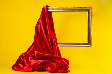 Levitating golden frame, being unveiled with a red satin cloth, isolated on yellow background