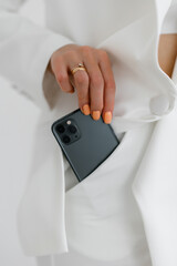 Girl pulls out a fancy green mobile phone from her white trouser pocket. 
Girl holding smartphone in trouser pocket. At close range. Technology. Modern, casual style.