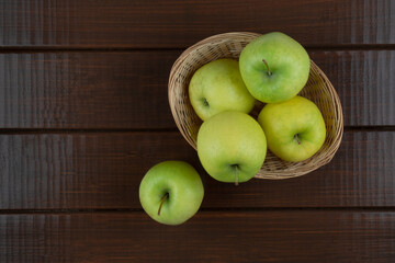 Green apples in a basket on a wooden table, top view, copy space