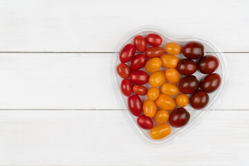 mixed tomatoes in a heart-shaped bowl on a white table, top view, copy space