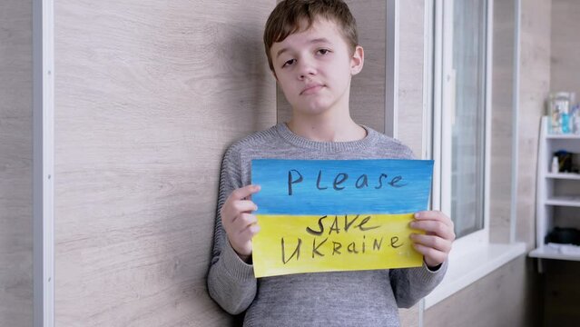 Child Holds a Banner with a Blue and Yellow Flag, Message Please Save Ukraine. Sad boy calling protests against the military conflict between Russia and Ukraine. Text with a call to stop the war.