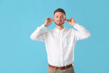 Young man putting ear plugs on blue background