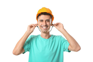 Smiling young builder in hardhat putting earplugs on white background