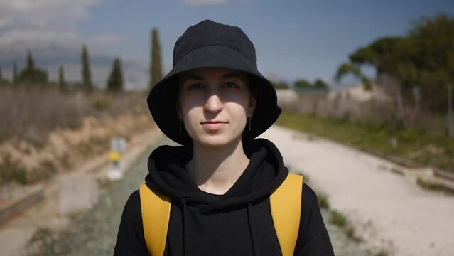 a teenage girl in black hat in golden earrings in the shape of a cross standing near the railway. Medium shot