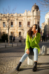 Young woman listening music with smartphone on the street and holding takeaway coffee