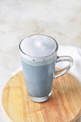 Wooden board with glass cup of delicious Charcoal Latte on light background
