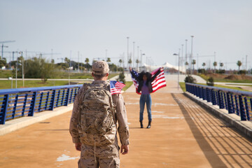 Naklejka premium African American woman with American flag, waiting for her partner, an American soldier who has just arrived from a mission. Concept army, missions, military, war. Selective focus on the soldier.
