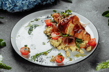 Delicious croissant sandwich with ham, cheese and scrambled eggs on plate served