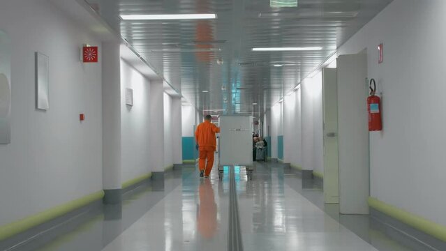 Man Carrying A Food Delivery Cart Down The Hospital Corridor