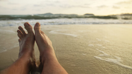 The barefoot man feet relaxed are lying on the sandy beach and washed by the water and foam of the ocean. Concept relax tropical resort traveling happy summer holiday