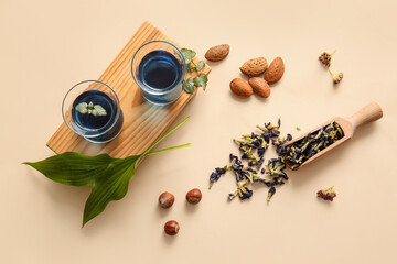 Composition with cups of blue tea, nuts and dried butterfly pea flowers on color background