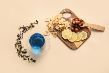 Composition with cup of blue tea, dried fruits and butterfly pea flowers on color background