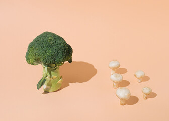 Green broccoli versus mushrooms on an orange background. Minimal layout healthy food concept.