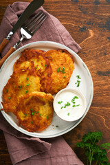 Potato pancakes. Fried homemade potato pancakes or latkes with cream and green onions in rustic plate on old wooden brawn table background. Rustic style. Healthy food. Top view.