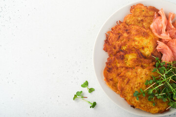 Potato pancakes. Fried homemade potato pancakes or latkes with cream, green onions, microgreens, red salmon and sauce in rustic plate on white table background. Rustic style. Healthy food. Top view.