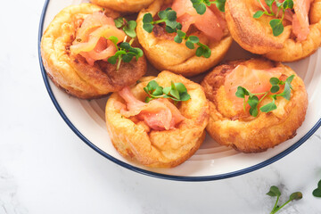 Yorkshire pudding. Traditional English Yorkshire pudding with salmon and radish microgreens side dish on white plate and light grey background table. Top view.