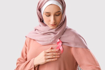 Muslim woman with pink ribbon on light background. Breast cancer awareness concept
