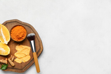 Wooden board with ingredients for turmeric mask and makeup brush on light background