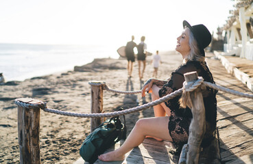 Fototapeta premium Happy cheerful model in stylish hat smiling during leisure time at sunny beach, joyful female dressed in bikini swimwear enjoying tropical vacations for recreation and sunbathing in Indonesia